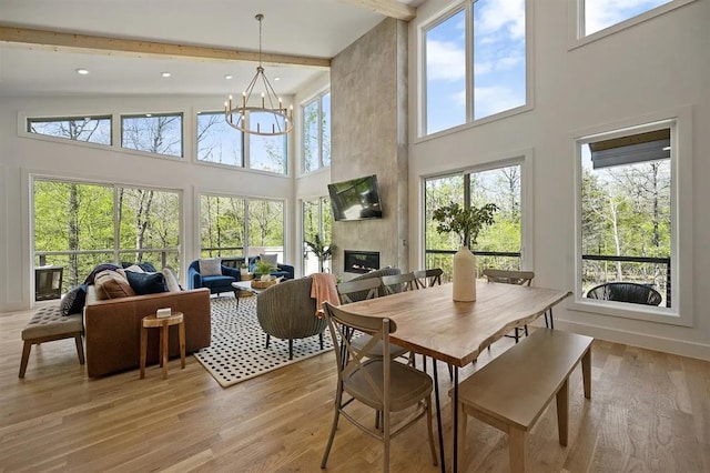 dining room featuring a large fireplace, light hardwood / wood-style flooring, beamed ceiling, high vaulted ceiling, and a notable chandelier