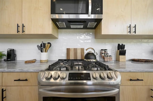 kitchen with decorative backsplash, light brown cabinets, light stone countertops, and appliances with stainless steel finishes