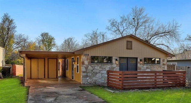 view of front of home featuring a carport, stone siding, fence, and concrete driveway