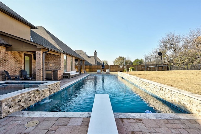 view of pool with an in ground hot tub, pool water feature, a diving board, a yard, and a trampoline