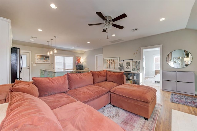 living room featuring ceiling fan with notable chandelier, lofted ceiling, sink, and light hardwood / wood-style flooring