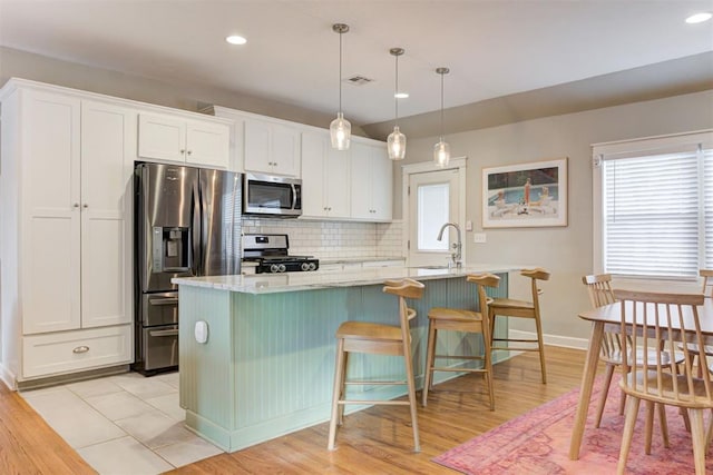 kitchen featuring hanging light fixtures, stainless steel appliances, light hardwood / wood-style flooring, and white cabinetry