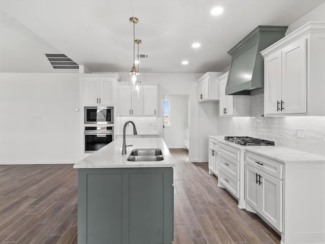 kitchen featuring stainless steel appliances, a kitchen island with sink, sink, wood-type flooring, and hanging light fixtures