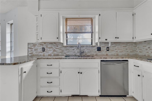 kitchen with stainless steel dishwasher, dark stone counters, sink, white cabinetry, and light tile patterned flooring