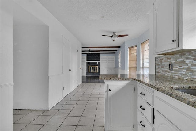 kitchen featuring a brick fireplace, ceiling fan, a textured ceiling, white cabinetry, and kitchen peninsula