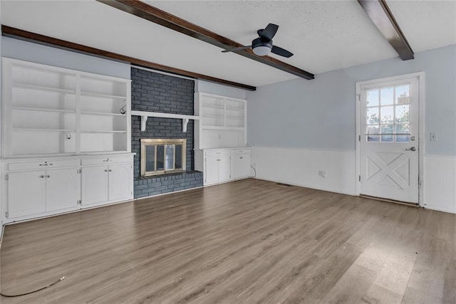 unfurnished living room with a brick fireplace, a textured ceiling, ceiling fan, beamed ceiling, and light hardwood / wood-style floors