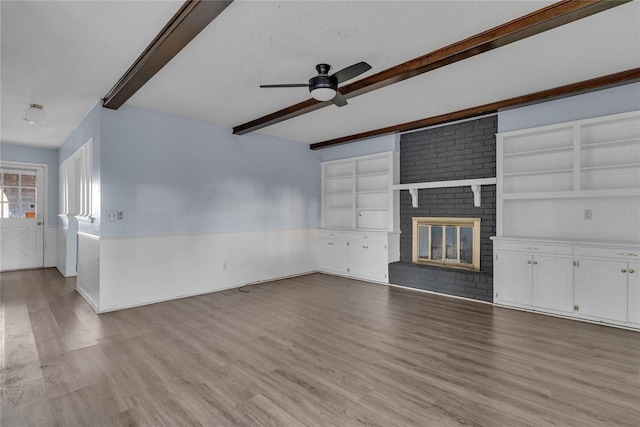 unfurnished living room with light hardwood / wood-style flooring, ceiling fan, a textured ceiling, a fireplace, and beam ceiling