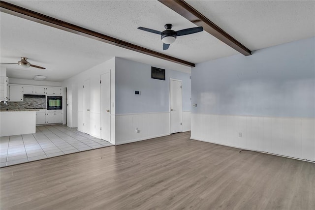 unfurnished living room with ceiling fan, beamed ceiling, a textured ceiling, and light wood-type flooring