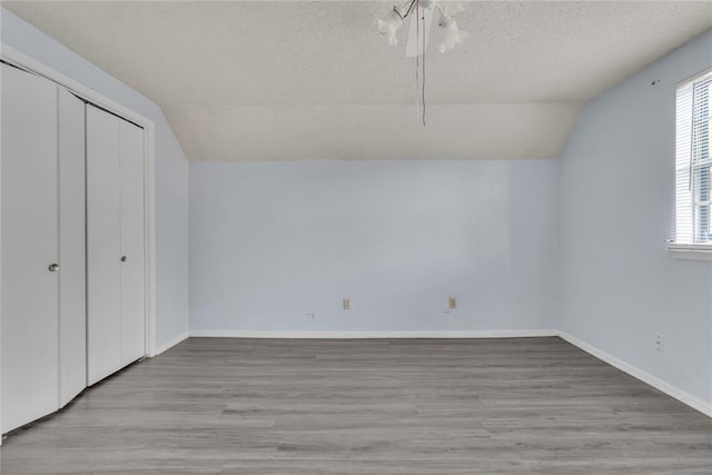 unfurnished bedroom with a textured ceiling, light hardwood / wood-style flooring, and vaulted ceiling