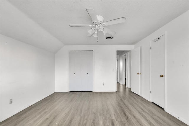 unfurnished bedroom with a textured ceiling, light wood-type flooring, vaulted ceiling, and ceiling fan