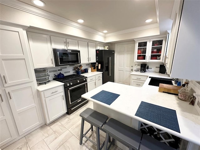 kitchen with black appliances, decorative backsplash, ornamental molding, white cabinetry, and kitchen peninsula