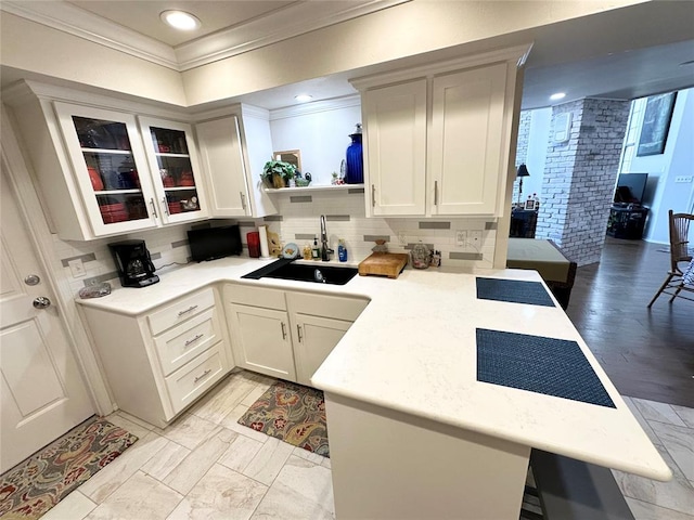 kitchen featuring kitchen peninsula, light wood-type flooring, crown molding, sink, and white cabinetry