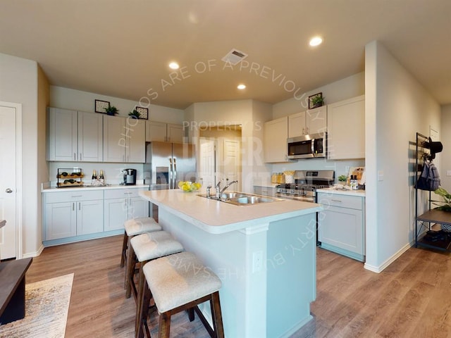 kitchen with a center island with sink, white cabinets, sink, light wood-type flooring, and appliances with stainless steel finishes