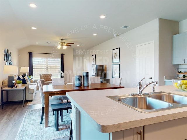 kitchen featuring ceiling fan, sink, hardwood / wood-style floors, an island with sink, and vaulted ceiling