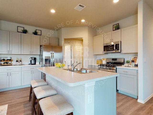 kitchen featuring a kitchen bar, stainless steel appliances, sink, light hardwood / wood-style floors, and an island with sink