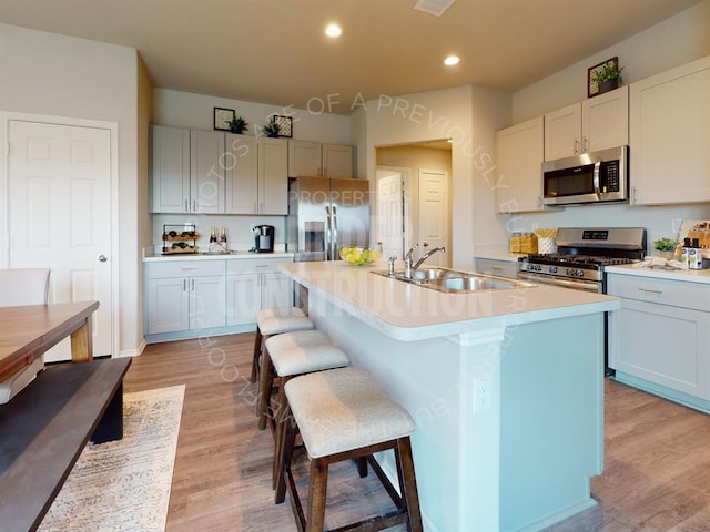 kitchen featuring a kitchen island with sink, sink, appliances with stainless steel finishes, light hardwood / wood-style floors, and a breakfast bar area