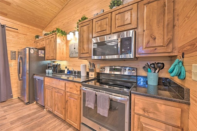 kitchen with wood walls, sink, light hardwood / wood-style flooring, vaulted ceiling, and stainless steel appliances