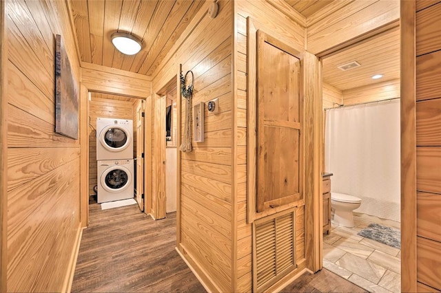 hall featuring wooden ceiling, stacked washing maching and dryer, dark wood-type flooring, and wood walls