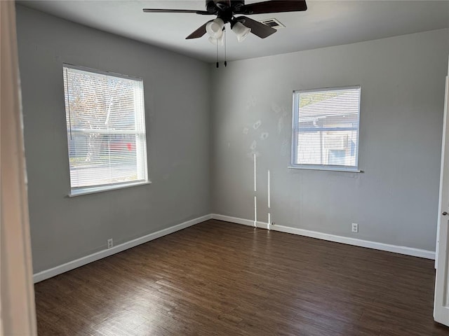 empty room featuring ceiling fan, dark wood-type flooring, and a healthy amount of sunlight