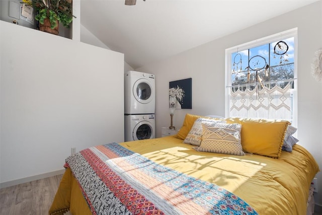 bedroom with wood-type flooring, vaulted ceiling, and stacked washer / dryer