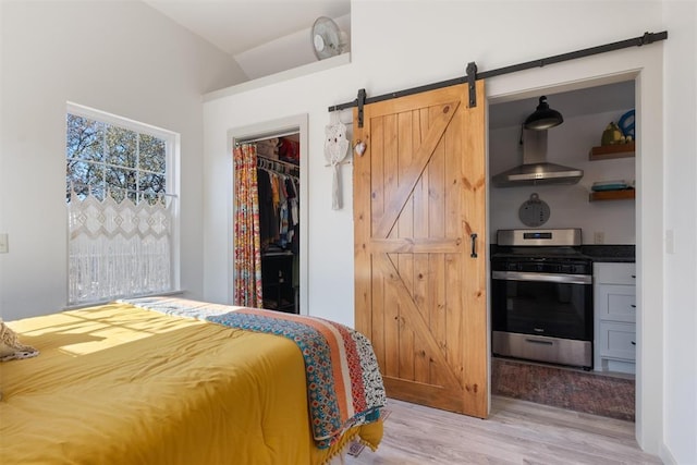 bedroom with a walk in closet, a barn door, light hardwood / wood-style floors, a closet, and lofted ceiling