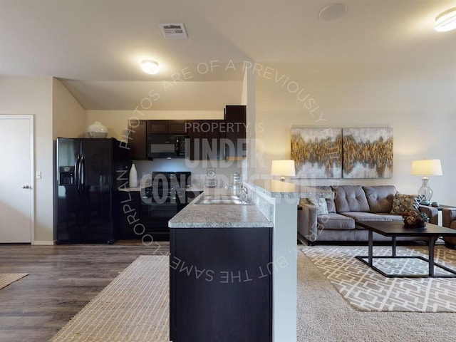 kitchen featuring dark brown cabinetry, sink, dark hardwood / wood-style floors, kitchen peninsula, and black appliances