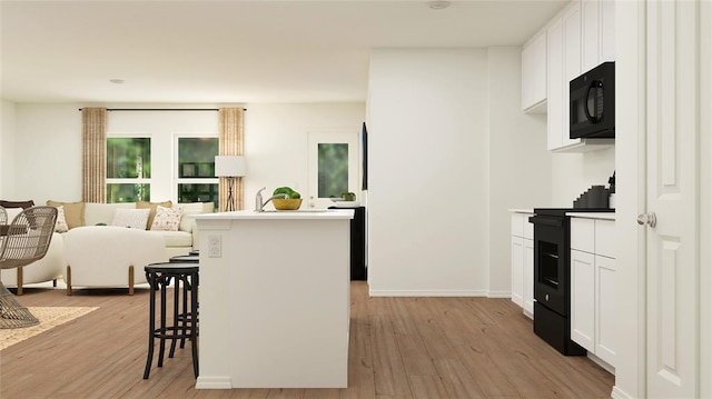 kitchen with black appliances, light hardwood / wood-style flooring, white cabinets, a kitchen island, and a breakfast bar area