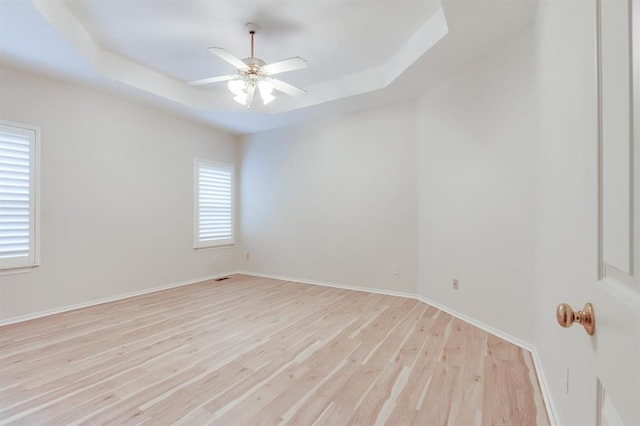 empty room with a raised ceiling, light hardwood / wood-style flooring, and a wealth of natural light