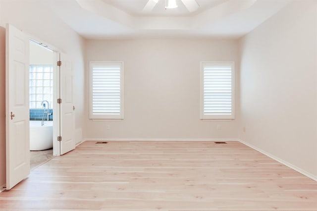 empty room with a raised ceiling, ceiling fan, and light hardwood / wood-style flooring