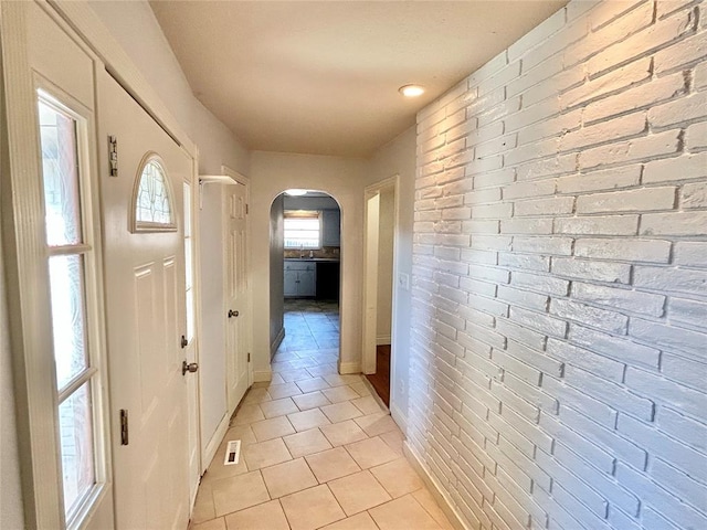 corridor featuring brick wall and light tile patterned flooring