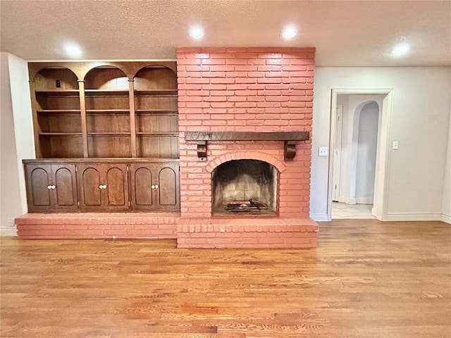 unfurnished living room with a textured ceiling, light hardwood / wood-style floors, and a brick fireplace