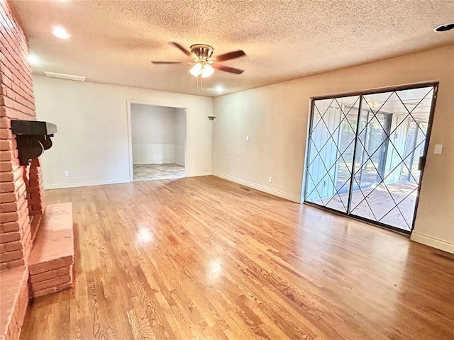 unfurnished living room with ceiling fan, light hardwood / wood-style flooring, a textured ceiling, and a brick fireplace