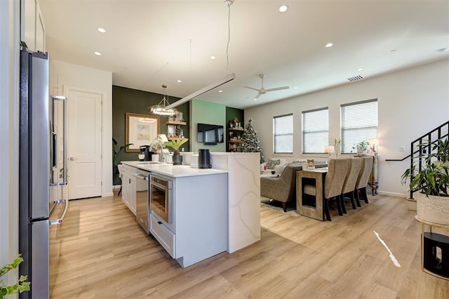 kitchen with pendant lighting, a kitchen island with sink, white cabinets, ceiling fan, and light hardwood / wood-style floors