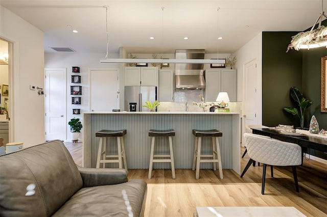 kitchen with stainless steel fridge with ice dispenser, light wood-type flooring, hanging light fixtures, and a kitchen breakfast bar