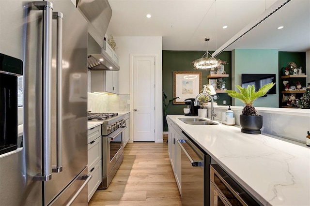 kitchen with high quality appliances, sink, light wood-type flooring, decorative light fixtures, and white cabinetry