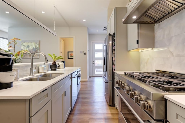 kitchen with sink, stainless steel appliances, light stone counters, light hardwood / wood-style flooring, and exhaust hood