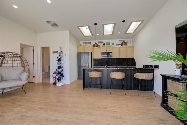 kitchen featuring decorative light fixtures, a kitchen bar, light wood-type flooring, and stainless steel appliances