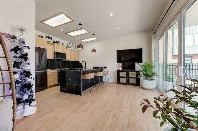 kitchen featuring black refrigerator, light wood-type flooring, tasteful backsplash, a breakfast bar, and hanging light fixtures