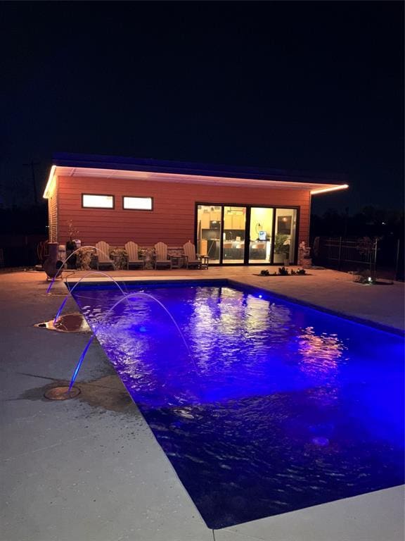 pool at twilight featuring pool water feature and a patio