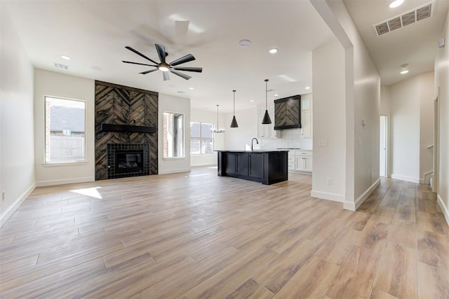 unfurnished living room with light wood-type flooring, a large fireplace, a wealth of natural light, and sink