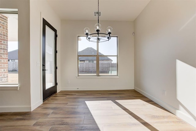 unfurnished dining area with wood-type flooring, an inviting chandelier, and french doors