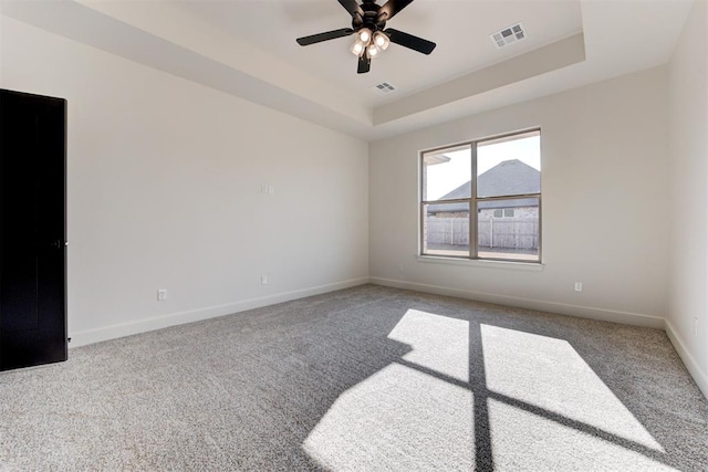 empty room featuring a raised ceiling, light carpet, and ceiling fan