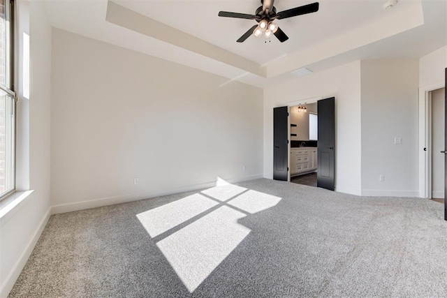 unfurnished bedroom with carpet, a tray ceiling, ceiling fan, and ensuite bathroom