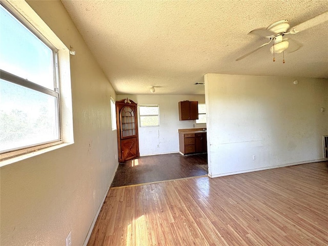 unfurnished living room with a textured ceiling, wood finished floors, a ceiling fan, and baseboards