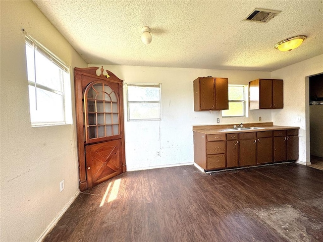 kitchen featuring a textured ceiling, dark wood finished floors, a sink, light countertops, and baseboards