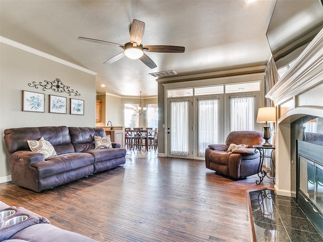 living room with a fireplace, dark wood-type flooring, ceiling fan with notable chandelier, and ornamental molding