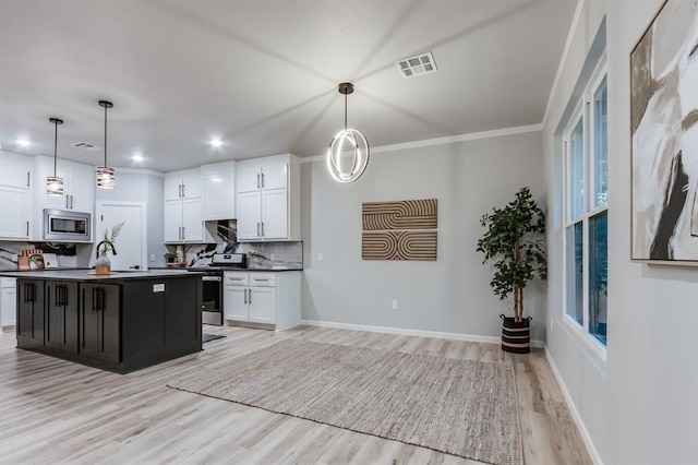 kitchen featuring white cabinets, a center island with sink, decorative backsplash, appliances with stainless steel finishes, and decorative light fixtures