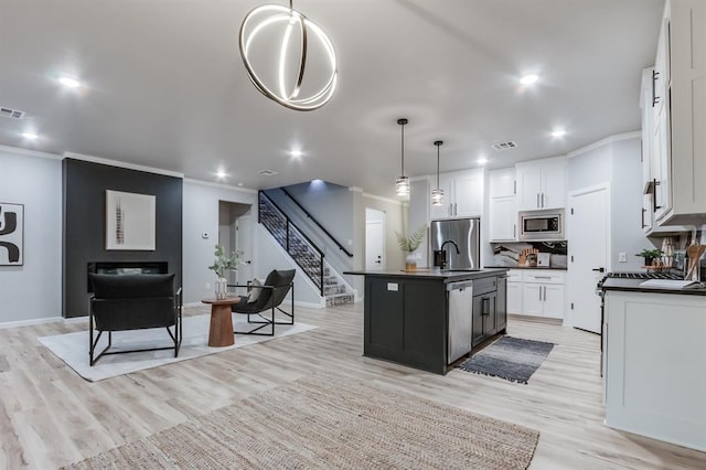 kitchen featuring pendant lighting, light hardwood / wood-style flooring, an island with sink, appliances with stainless steel finishes, and white cabinetry