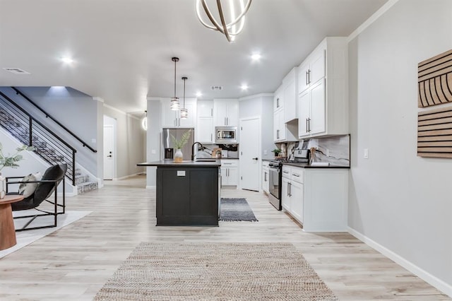 kitchen featuring white cabinets, decorative light fixtures, stainless steel appliances, and an island with sink