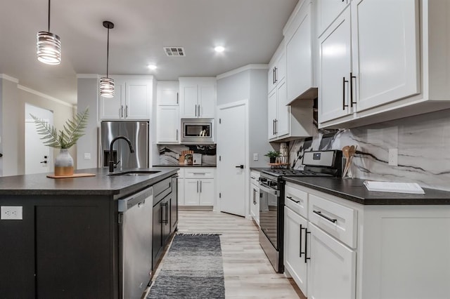 kitchen featuring hanging light fixtures, backsplash, a kitchen island with sink, white cabinets, and appliances with stainless steel finishes